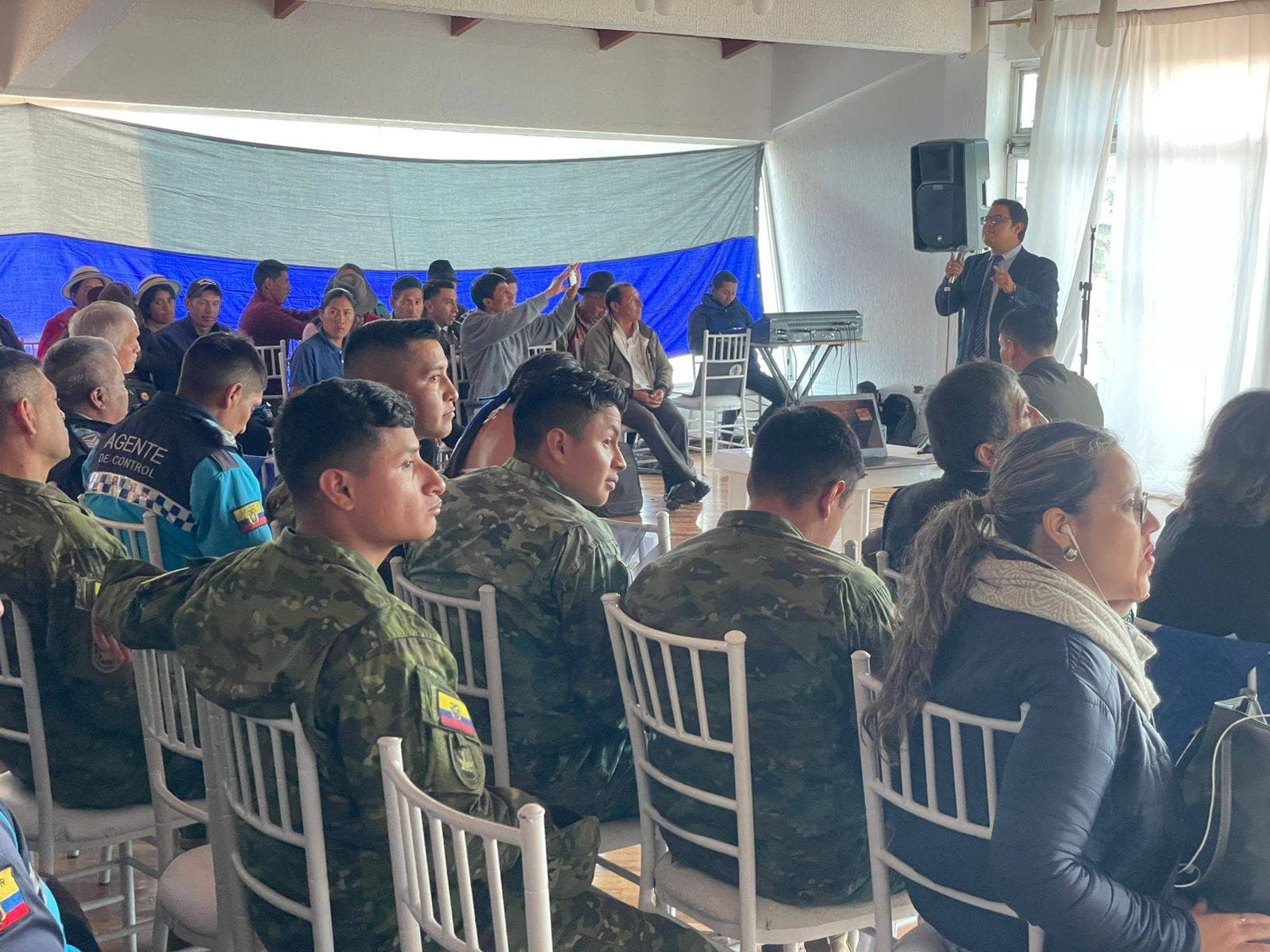 Un hombre da un discurso ante militares y civiles en un salón de actos.
