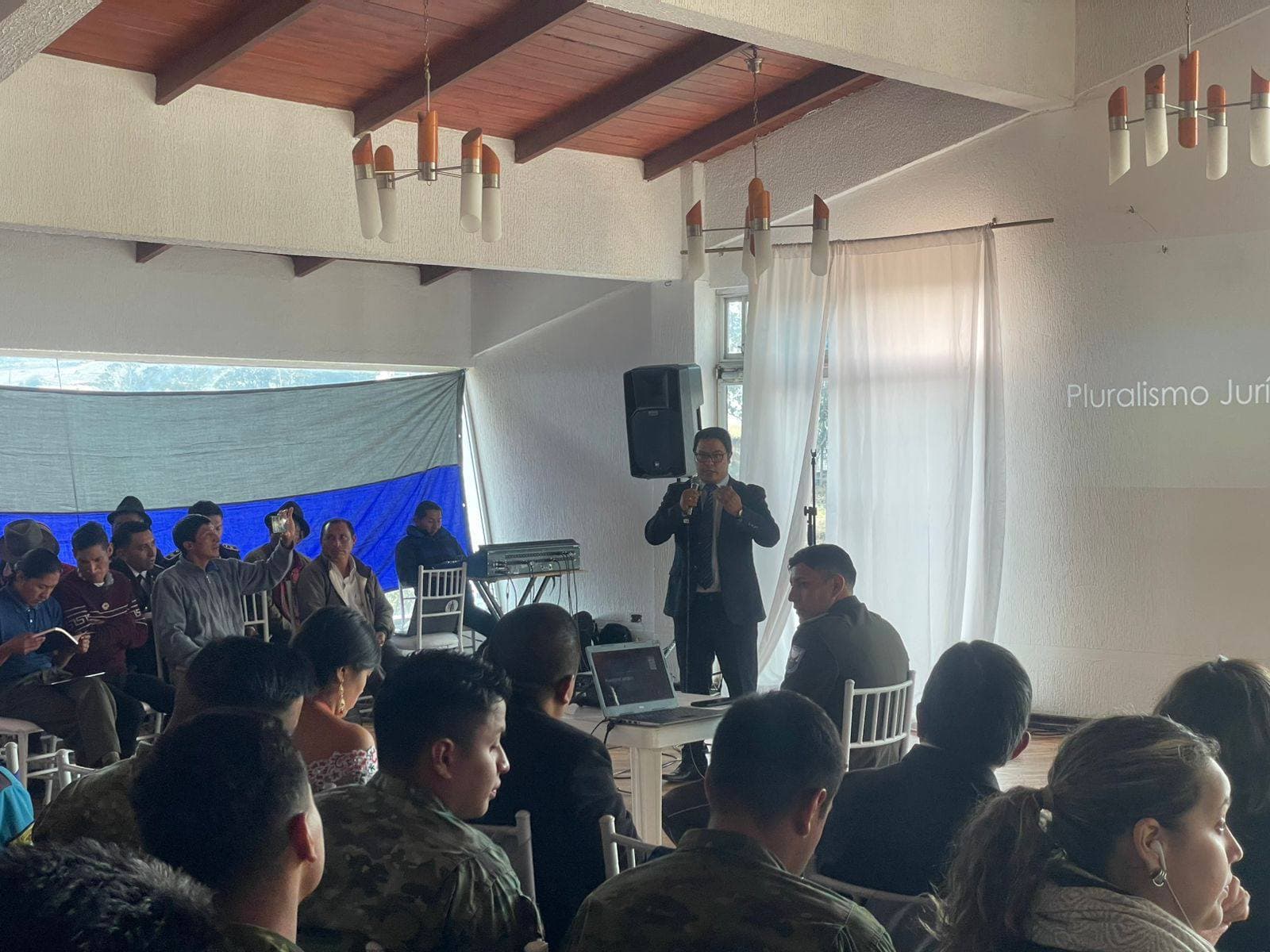 Conferencista de traje habla sobre pluralismo jurídico ante una audiencia con militares y civiles.